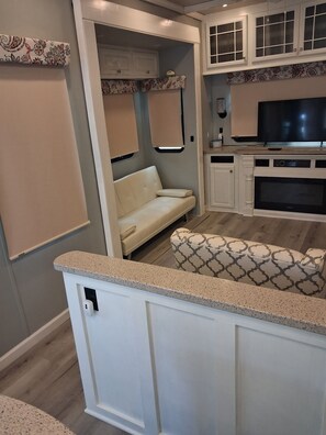 Ein kompaktes Wohnmobil-Interieur mit einer Küchenzeile, einer Sitzecke und einem Fernseher.