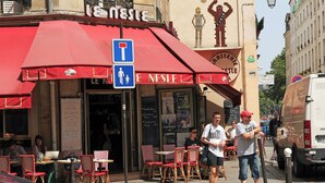 Un café con mesas al aire libre, un letrero de estacionamiento para discapacitados en azul y un menú en una pizarra.