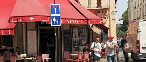 Un café avec une terrasse, un panneau bleu indiquant une place de stationnement réservée aux personnes handicapées et un menu écrit à la craie.
