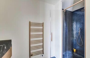 A bathroom with a shower, a towel rack, and a wall-mounted heater. - 3 bedroom apartment (Paris)