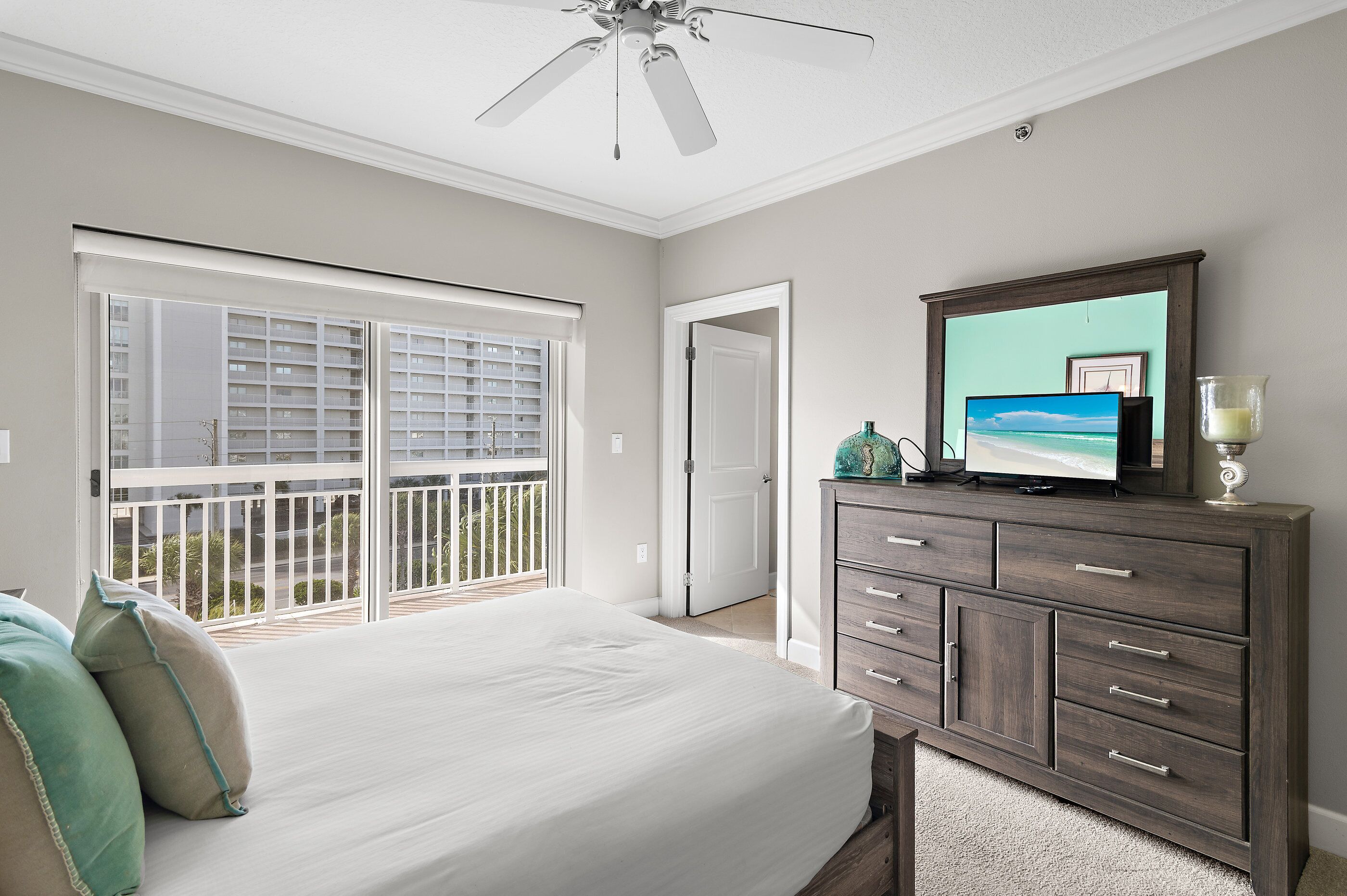 A bedroom with a bed, a dresser, a television, and a balcony.