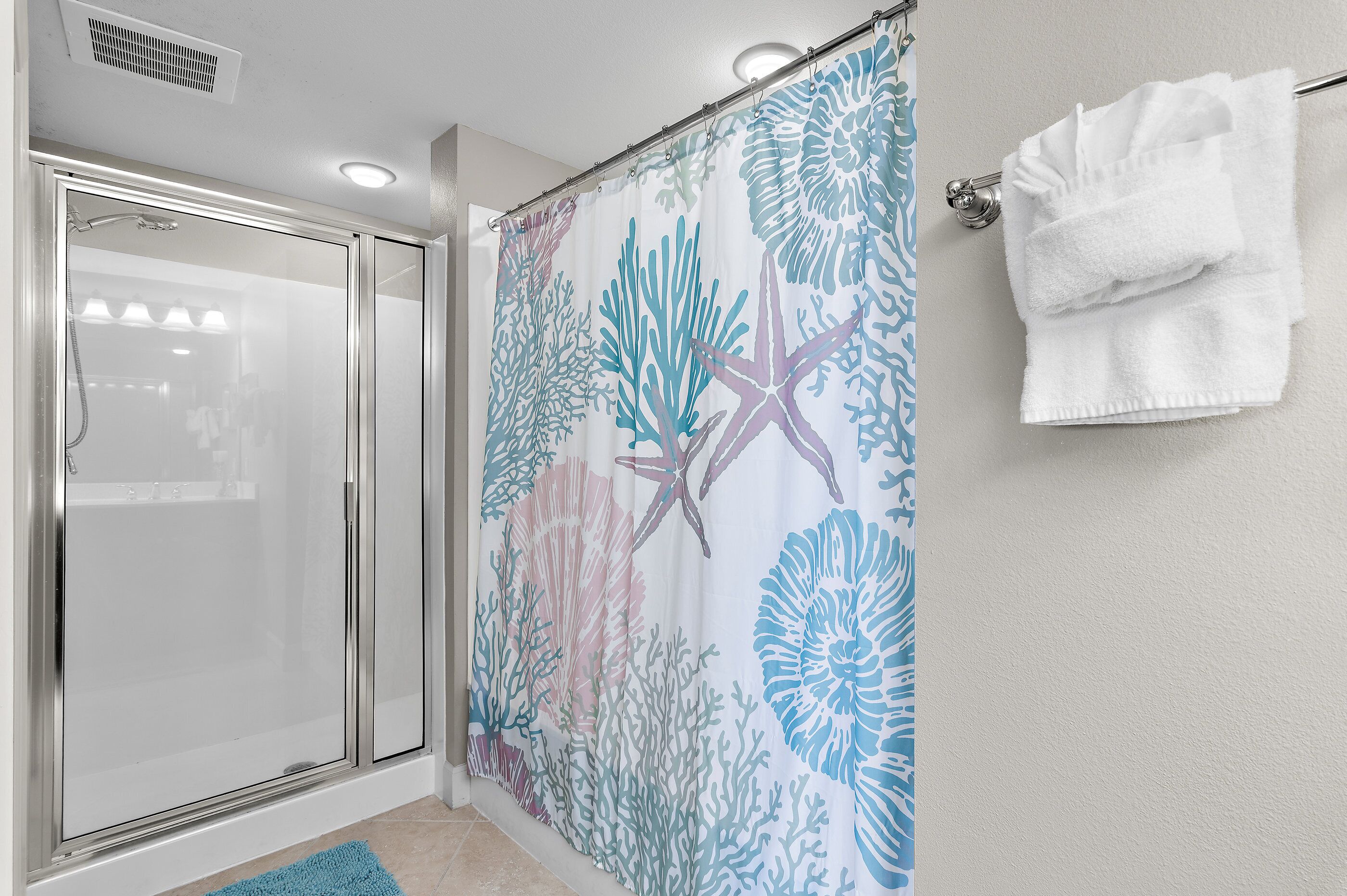 A shower with a glass door, a shower curtain with a marine life pattern, and a towel rack with a white towel.