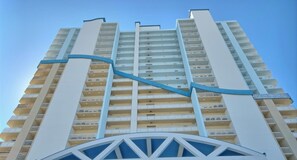 Ein Hochhaus mit zahlreichen Balkonen, einem markanten blauen Strukturelement und einem geometrischen Design am Sockel.