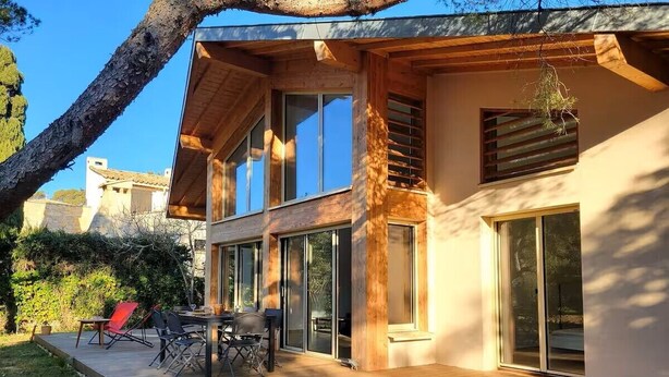 Ein modernes, zweistöckiges Haus mit einer Holzdiele, großen Fenstern und einer Terrasse.