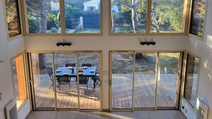 Ein Zimmer mit großen Fenstern, einer Glastür und Blick auf eine Terrassenanlage.