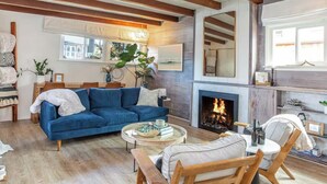 Ein Wohnzimmer mit Kamin, einem blauen Sofa, Holzbalken und Blick ins Freie.