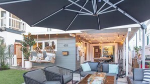 Eine Terrasse im Freien mit Korbmöbeln, einem Glastisch und einem großen Sonnenschirm.