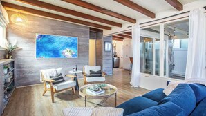Ein modernes Wohnzimmer mit Holzbalkendecke, einem großen Gemälde, einem blauen Sofa und einem Glastisch.
