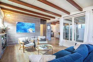 Ein modernes Wohnzimmer mit Holzbalkendecke, einem großen Gemälde, einem blauen Sofa und einem Glastisch.