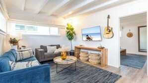 A living room with a blue sofa, a grey couch, a coffee table, a TV, a guitar, and a plant. - Walk to Beach,Shops and Restaurants,Beach Cottage! (Newport Beach)