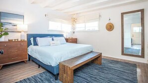 A bedroom with a bed, wooden bench, bedside tables, a mirror, and a wall-mounted light fixture. - Walk to Beach,Shops and Restaurants,Beach Cottage! (Newport Beach)