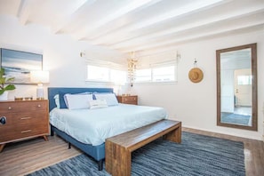 Ein Schlafzimmer mit Bett, Holzbank, Nachttischen, einem Spiegel und einer Wandleuchte.