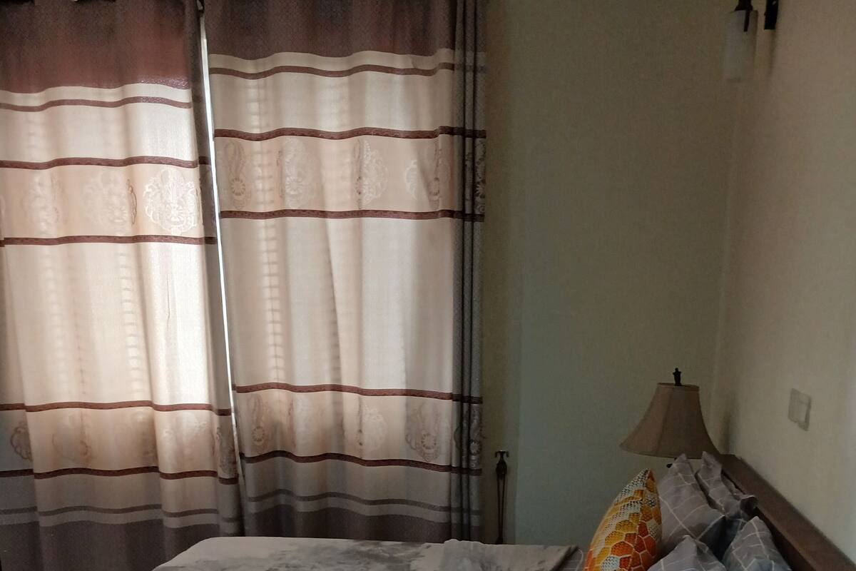 Una cama con una colcha gris, un cabecero de madera y una mesita de noche con una lámpara.