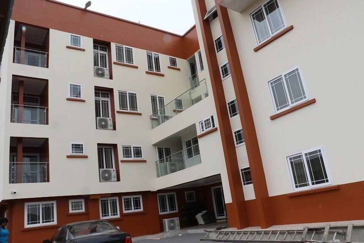 Un edificio de varios pisos con balcones, unidades de aire acondicionado y un coche estacionado al frente.