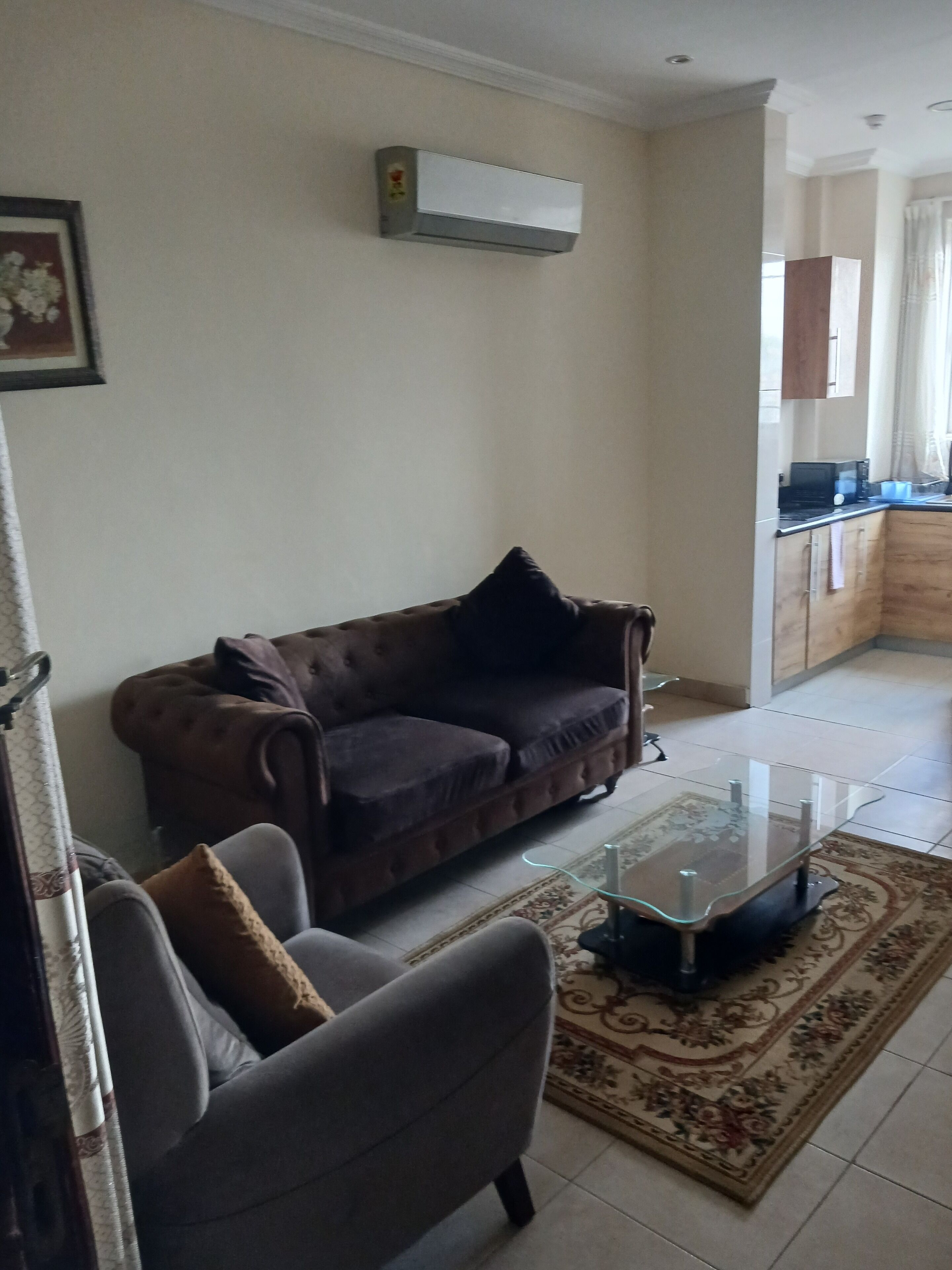 A living room with a sofa, a glass coffee table, and a kitchen in the background.