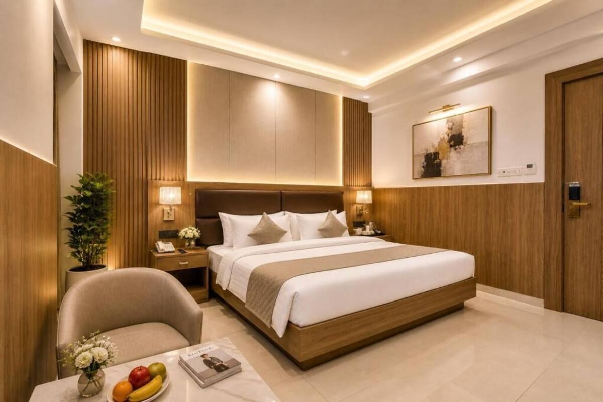 Una habitación de hotel moderna con una cama grande, mesitas de noche, una silla y una pequeña mesa con fruta y flores.