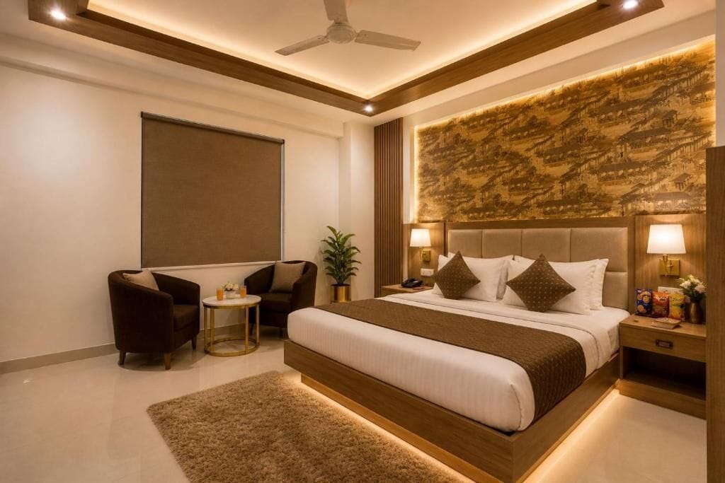 A modern hotel room with a large bed, two armchairs, a small side table, a ceiling fan, and a wall-mounted artwork.