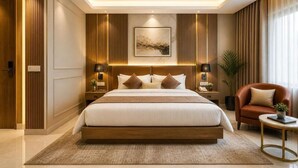 A modern hotel room with a large bed, bedside tables, a red armchair, and a view of the outdoors. - Hotel The Capital Stay (New Delhi)