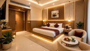 A modern hotel room with a large bed, bedside tables, a seating area, and a television. - Hotel The Capital Stay (New Delhi)
