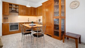 A kitchen with wooden cabinets, a dining table with chairs, a built-in oven, and a wall-mounted clock. - Holiday Home 'La Casa Di Leone Casa Sorella' with Sea View, Wi-Fi and Air Conditioning (Agkisaras)