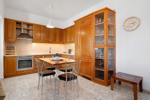 Una cocina con armarios de madera, una mesa de comedor con sillas, un horno empotrado y un reloj de pared.
