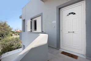 Una puerta blanca con un pequeño ventanal encima y un timbre en la pared.