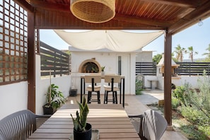 Un patio exterior con mesa y sillas, un horno de ladrillo y plantas en macetas.