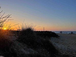 Uma praia com pôr do sol, dunas de areia e um deck de madeira.