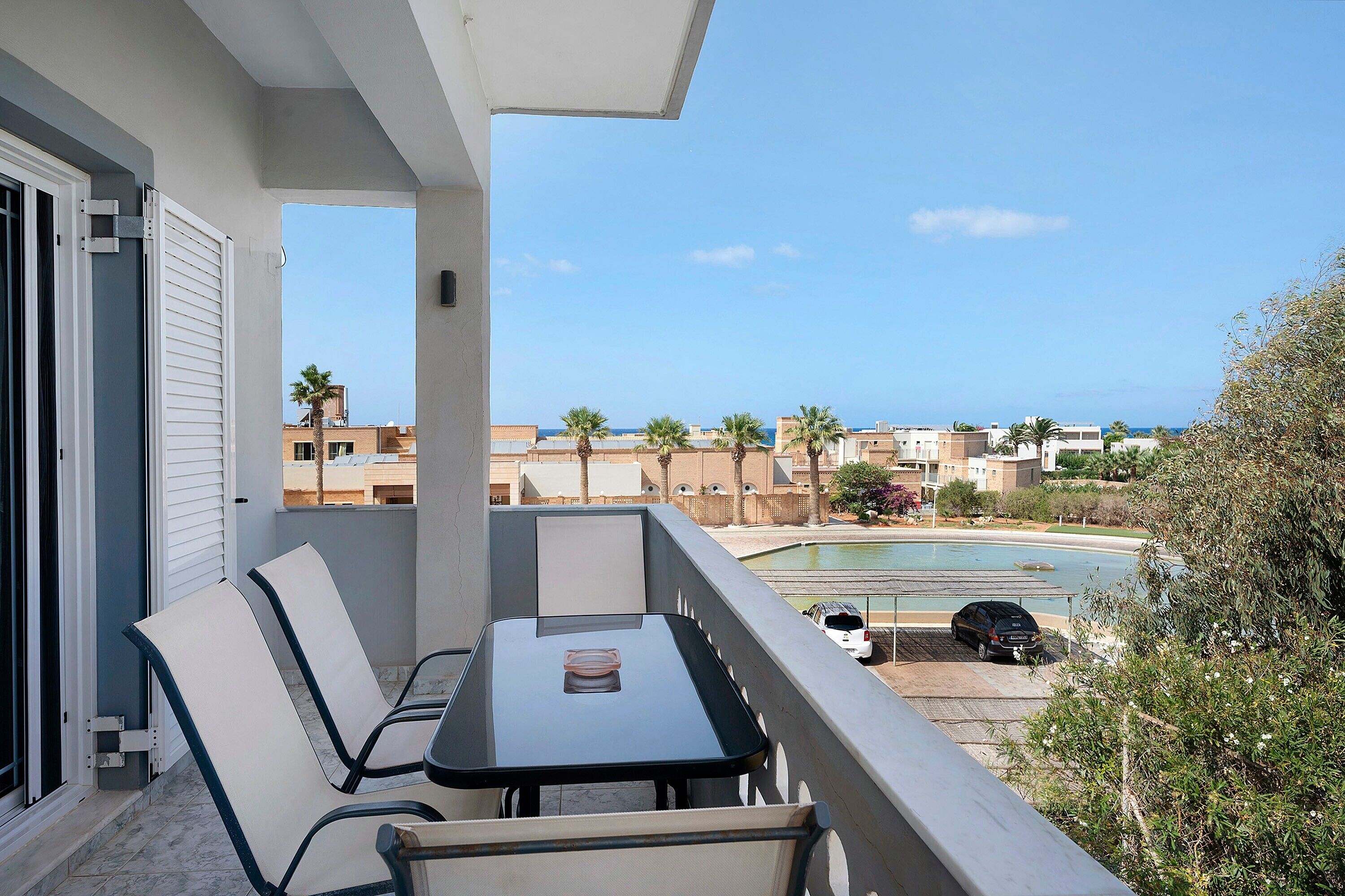 A balcony with a table and chairs, overlooking a swimming pool and a residential area.