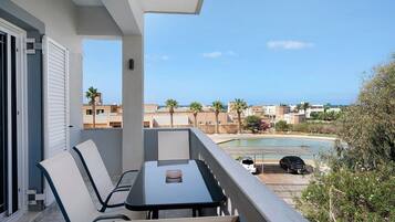 A balcony with a table and chairs, overlooking a swimming pool and a residential area.