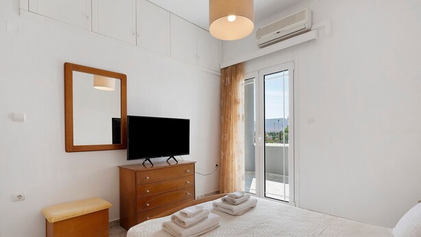 A hotel room with a bed, a television, a wooden dresser, a bench, and a large window with a view. - Holiday Home 'La Casa Di Leone Casa Sorella' with Sea View, Wi-Fi and Air Conditioning (Agkisaras)