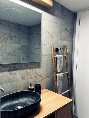 Ein Badezimmer mit einem großen Spiegel, einer Holzwaschkommode, einem schwarzen Waschbecken und einem Handtuchhalter mit Handtüchern.
