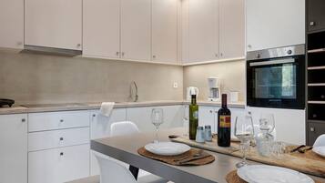 Een moderne keuken met witte kasten, een ingebouwde oven en een eethoek met borden, glazen en een fles.