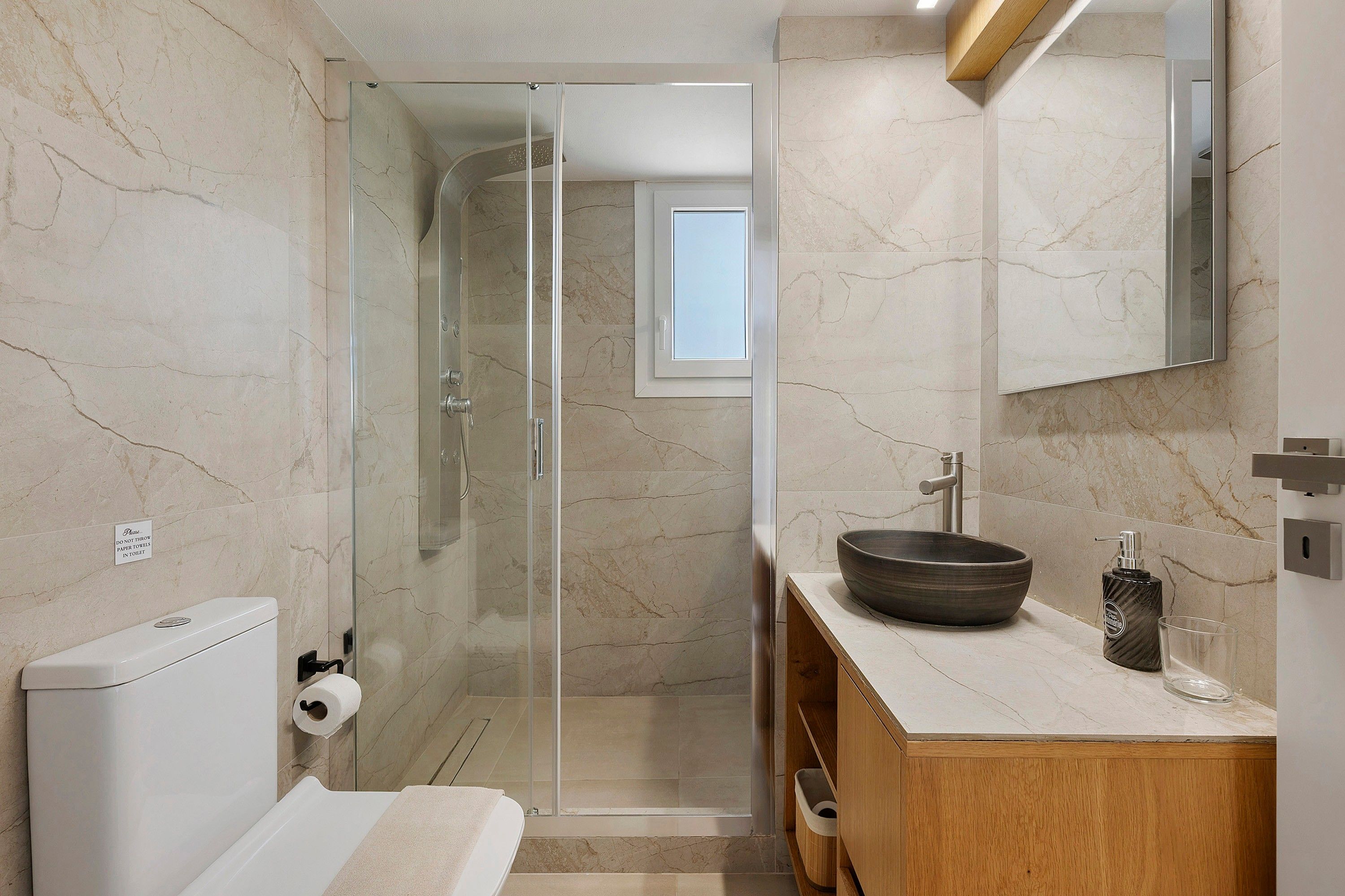 Une salle de bain moderne avec une douche à parois de verre, un meuble-lavabo en bois et un mur recouvert de carreaux de marbre.