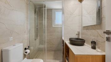 Une salle de bain moderne avec une douche à parois de verre, un meuble-lavabo en bois et un mur recouvert de carreaux de marbre.