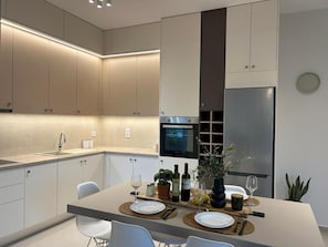 Uma cozinha moderna com eletrodomésticos embutidos, um espaço de refeições com uma mesa posta para dois e um relógio na parede.