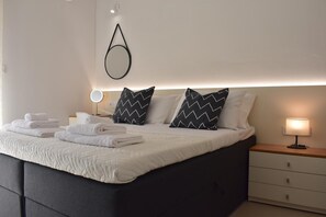 Ein ordentlich bezogenes Bett mit Kissen, einer Nachttischlampe und einem an der Wand befestigten Spiegel.