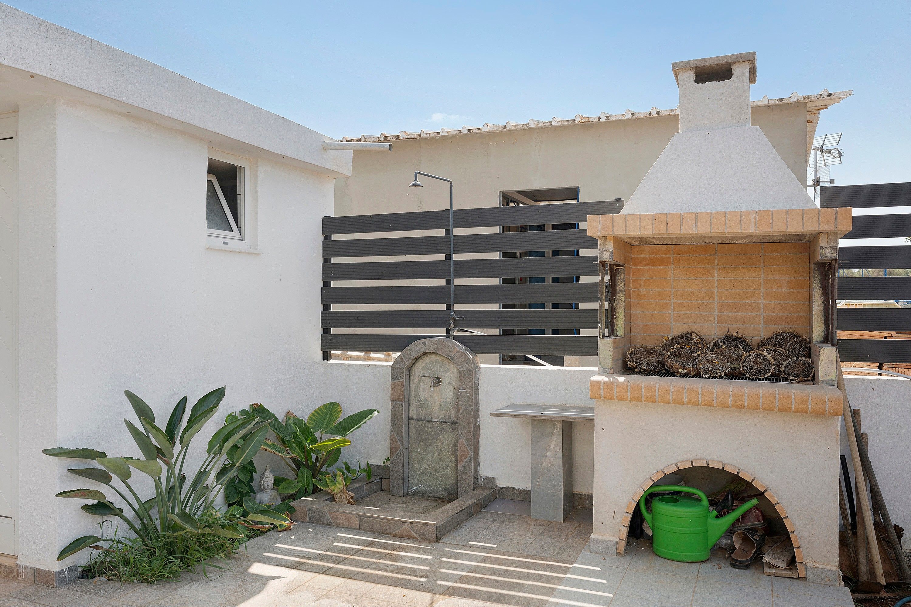 Eine Terrasse mit einem Ziegelofen, einer kleinen Buddha-Statue und einem grünen Gießkann.