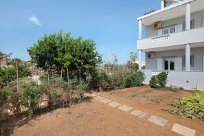 A modern two-story building with a garden area featuring a variety of plants and a stone pathway. - Apartment 'La Casa Di Leone - Gio' with Shared Terrace, Wi-Fi and Air Conditioning (Agkisaras)