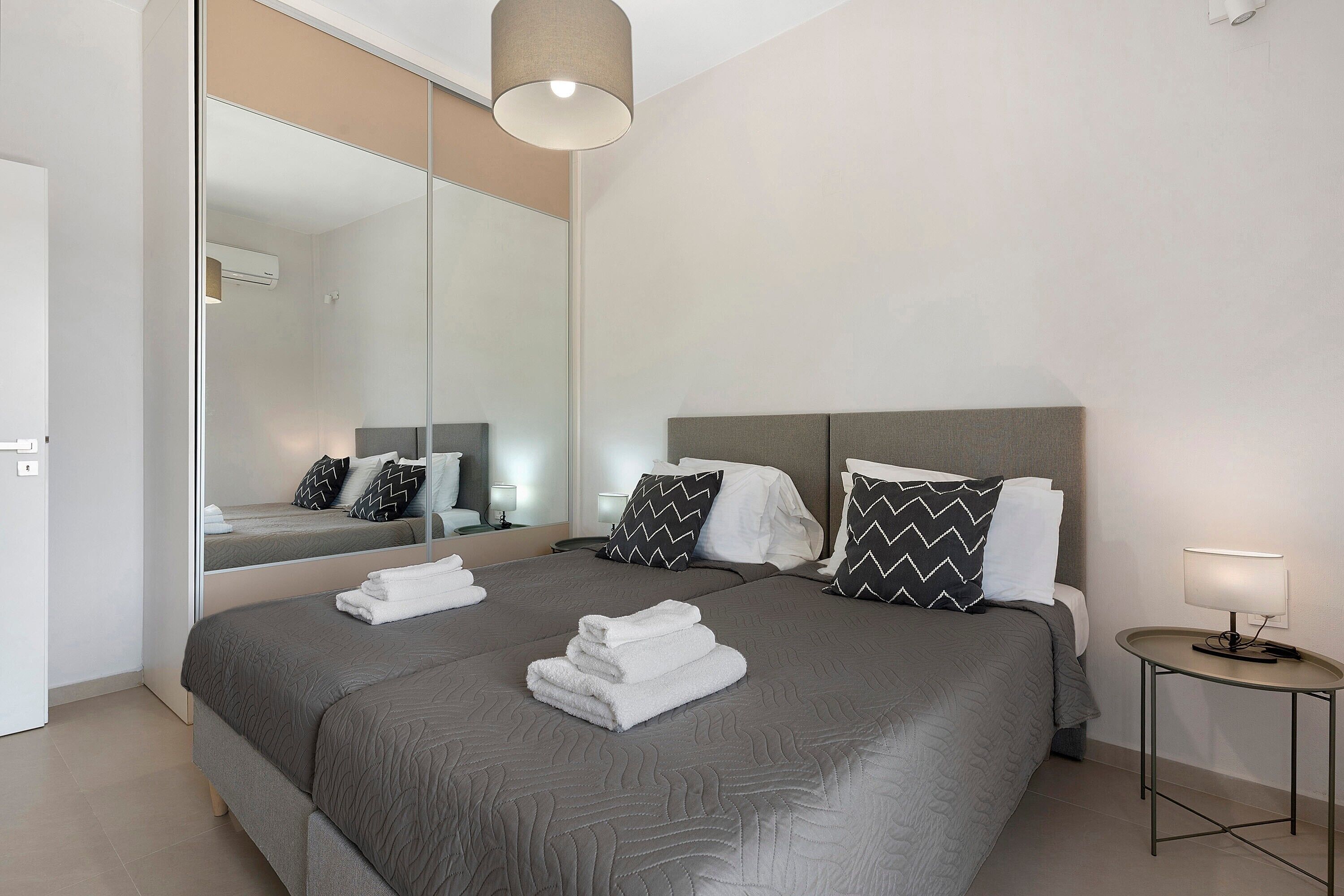 A modern hotel room with a large bed, a bedside table, a mirror, and a lamp.