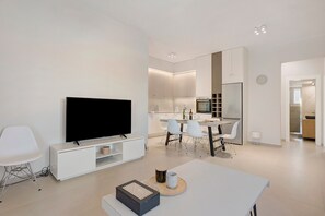 A modern living room with a flat-screen TV, a dining area with chairs, a kitchen with cabinets, and a clock on the wall. - Apartment 'La Casa Di Leone - Gio' with Shared Terrace, Wi-Fi and Air Conditioning (Agkisaras)