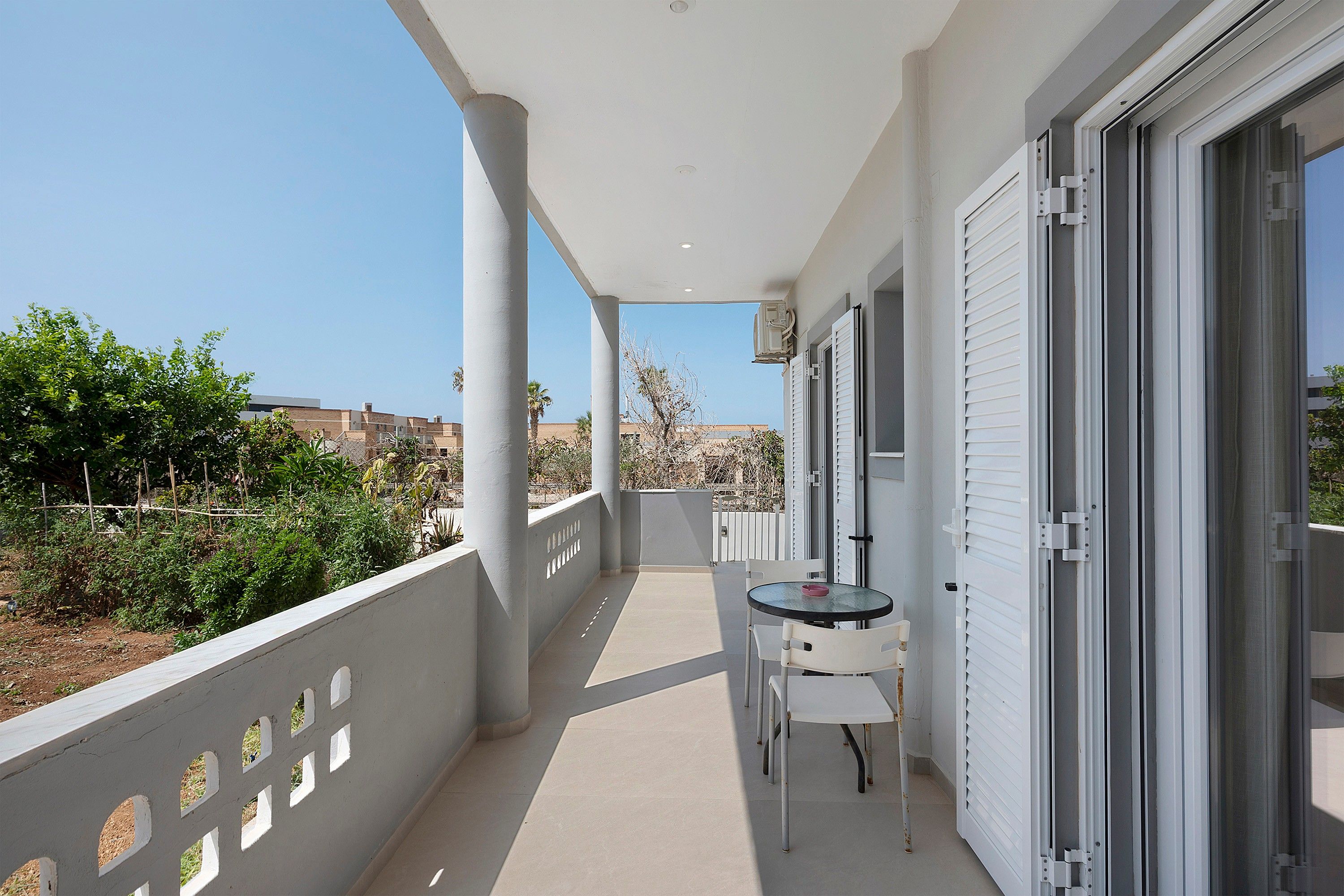 A balcony with a table and chairs, a sliding glass door, and a view of the surrounding area.
