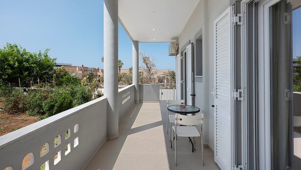 Un balcon avec une table et des chaises, une porte-fenêtre coulissante et une vue sur les environs.