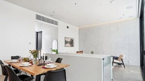 A modern dining area with a wooden table, black chairs, a white partition, and a view of the kitchen. - Smart Home. Cinema. Sauna. Sonos Audio (Espoo)