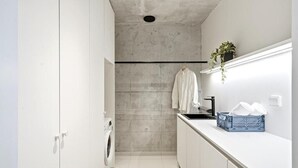 A narrow, modern kitchen with a washing machine, a hanging towel, and a blue basket on the counter. - Smart Home. Cinema. Sauna. Sonos Audio (Espoo)
