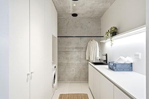 A narrow, modern kitchen with a washing machine, a hanging towel, and a blue basket on the counter. - Smart Home. Cinema. Sauna. Sonos Audio (Espoo)