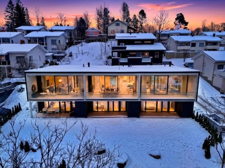 A modern house with large glass windows, a flat roof, and a snow-covered landscape.. Smart Home. Cinema. Sauna. Sonos Audio