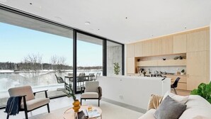 A modern living room with a large window, a sofa, a coffee table, and a kitchen area. - Smart Home. Cinema. Sauna. Sonos Audio (Espoo)
