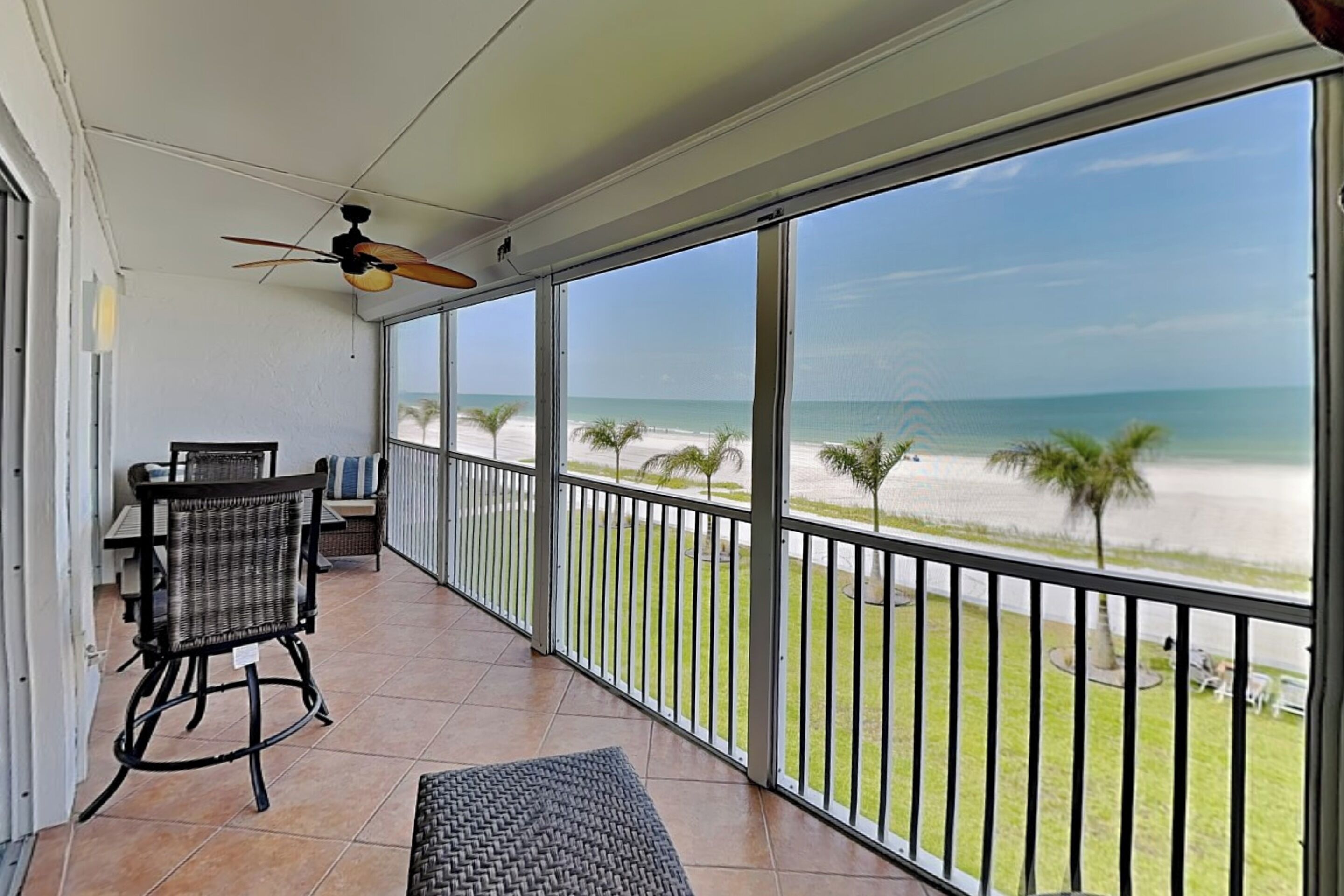 Un balcon avec vue sur la plage, un ventilateur de plafond et du mobilier d’extérieur.