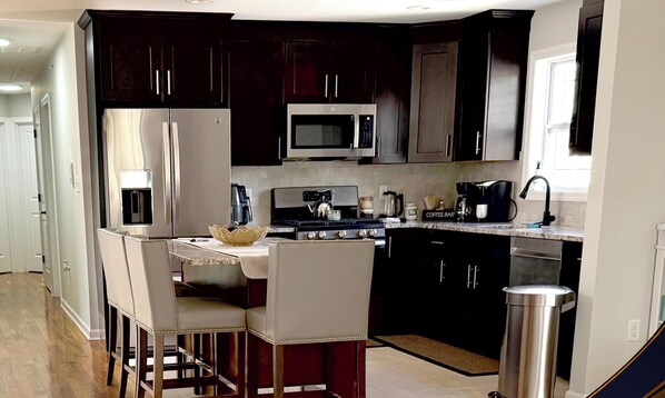 Una cocina moderna con armarios oscuros, electrodomésticos de acero inoxidable, una estación de café y una zona con taburetes de bar.